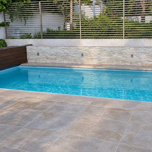 Piscina junto a una terraza de piedra, muro revestido y cierre horizontal